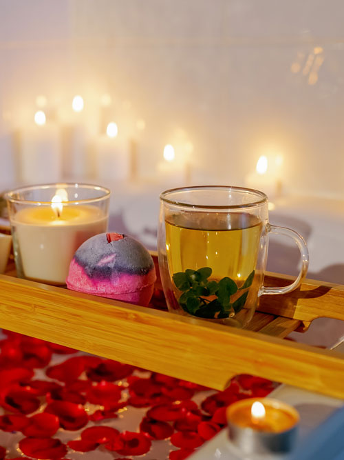 Herbal mint tea on bathtub tray with candles, lavender and salt .